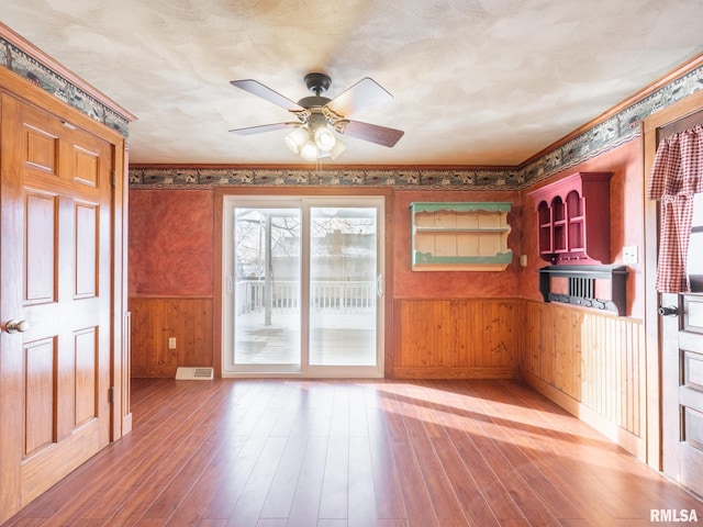 interior space featuring hardwood / wood-style flooring, ceiling fan, wood walls, and a textured ceiling