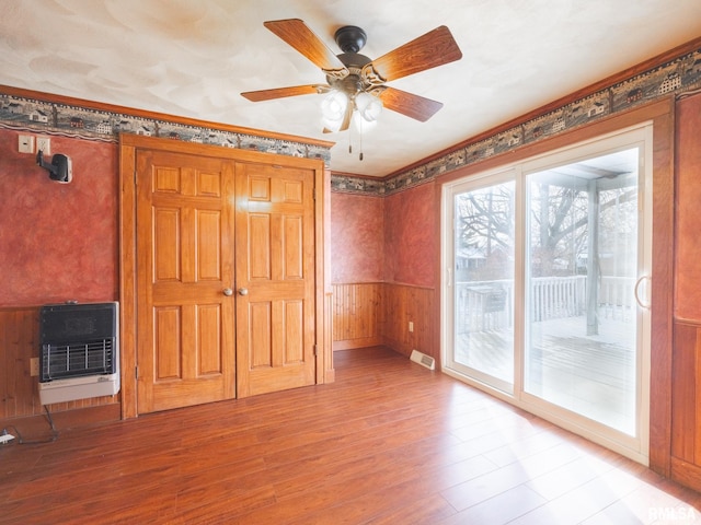 interior space with access to outside, wooden walls, ceiling fan, light hardwood / wood-style floors, and heating unit