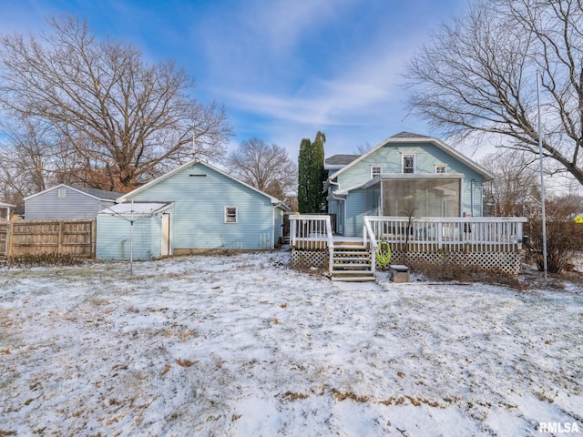 snow covered rear of property featuring a sunroom and a wooden deck