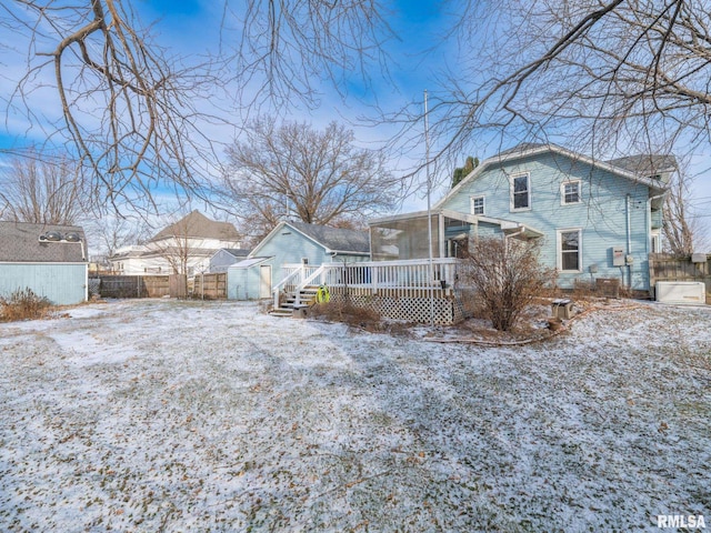 snow covered rear of property with a wooden deck, a sunroom, and a shed