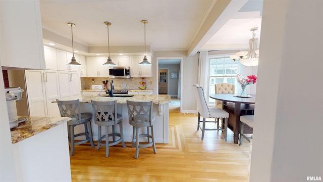 kitchen featuring light stone countertops, pendant lighting, white cabinets, and a kitchen breakfast bar