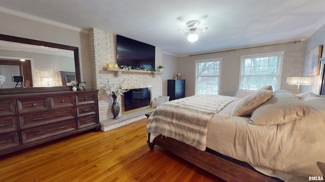 bedroom featuring a brick fireplace, ornamental molding, and light wood-type flooring