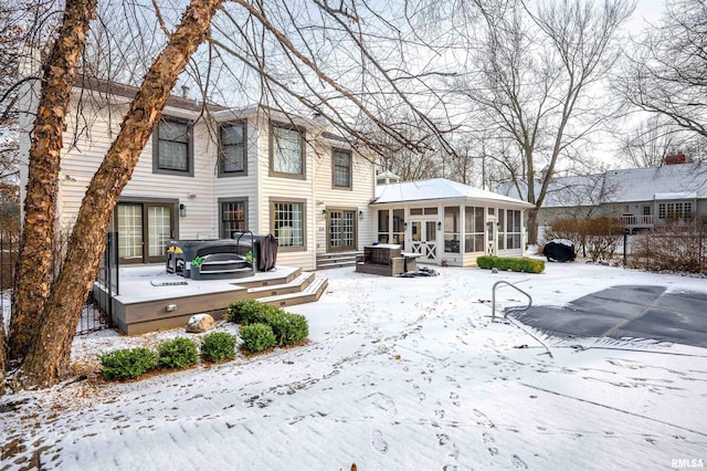 snow covered rear of property with a sunroom and a hot tub