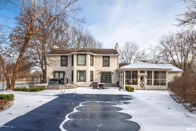 snow covered rear of property featuring a sunroom