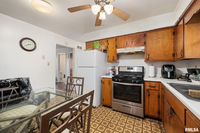 kitchen featuring ceiling fan, stainless steel gas range oven, sink, and white refrigerator