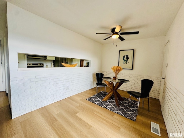 interior space featuring wood-type flooring, ceiling fan, and brick wall