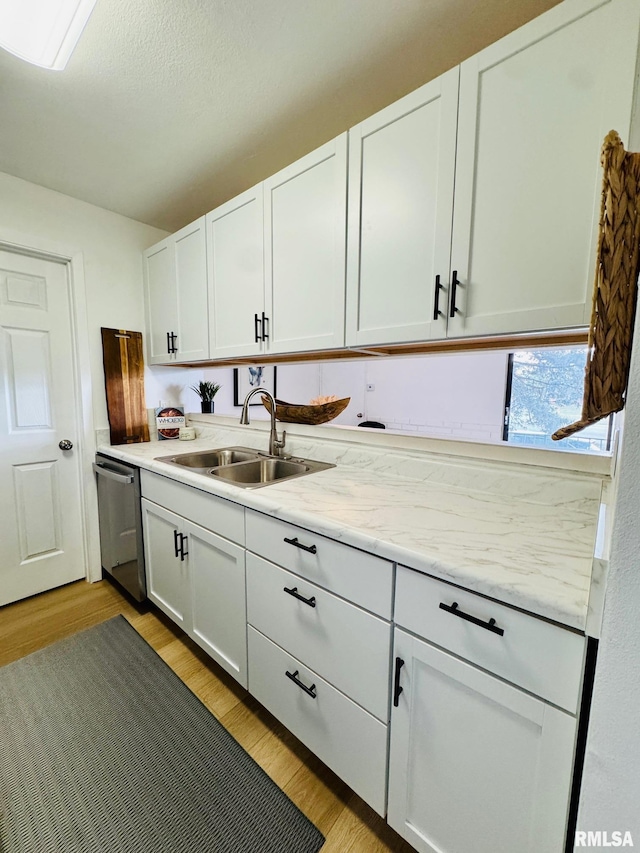 kitchen with sink, light stone counters, light hardwood / wood-style flooring, stainless steel dishwasher, and white cabinets