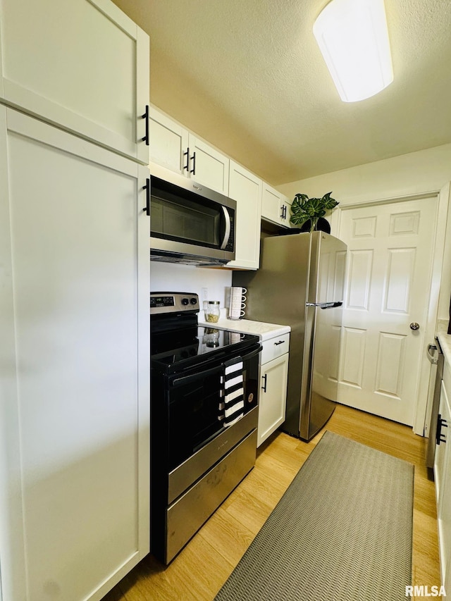 kitchen featuring a textured ceiling, light hardwood / wood-style floors, white cabinetry, and stainless steel appliances