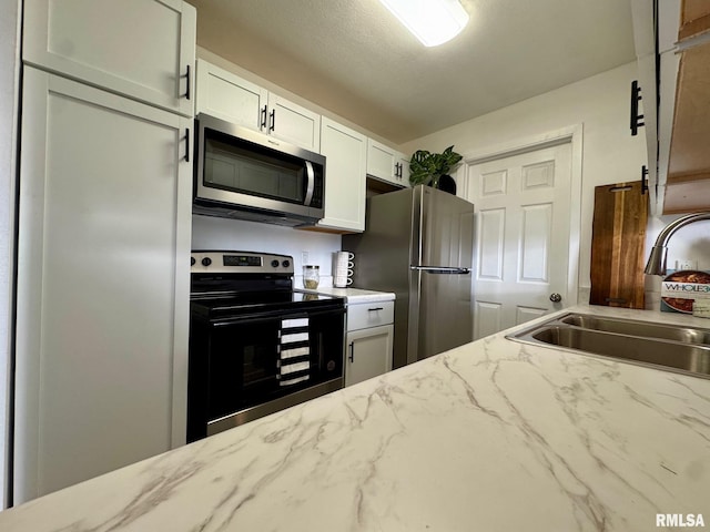 kitchen with light stone counters, a textured ceiling, stainless steel appliances, sink, and white cabinets