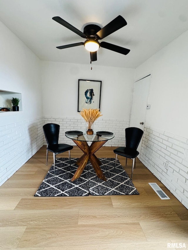 sitting room with hardwood / wood-style floors, ceiling fan, and brick wall