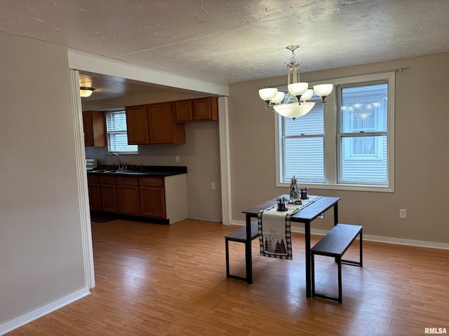 dining room featuring sink, light hardwood / wood-style floors, a textured ceiling, and an inviting chandelier