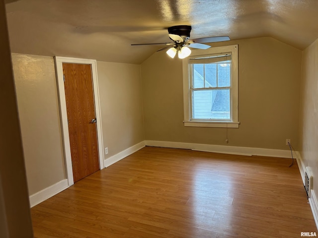 additional living space featuring a textured ceiling, light hardwood / wood-style floors, vaulted ceiling, and ceiling fan