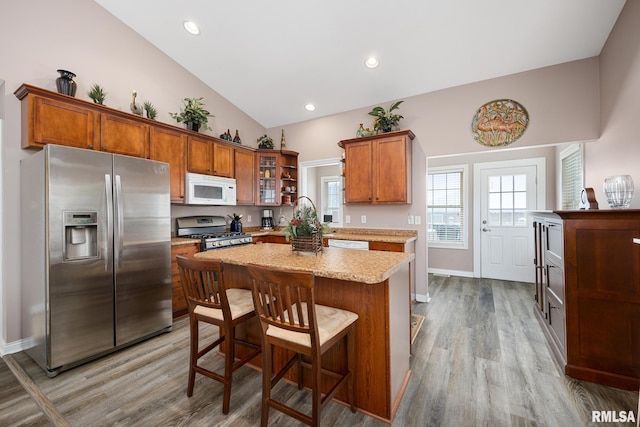 kitchen with light stone countertops, a breakfast bar, stainless steel appliances, light hardwood / wood-style flooring, and a kitchen island