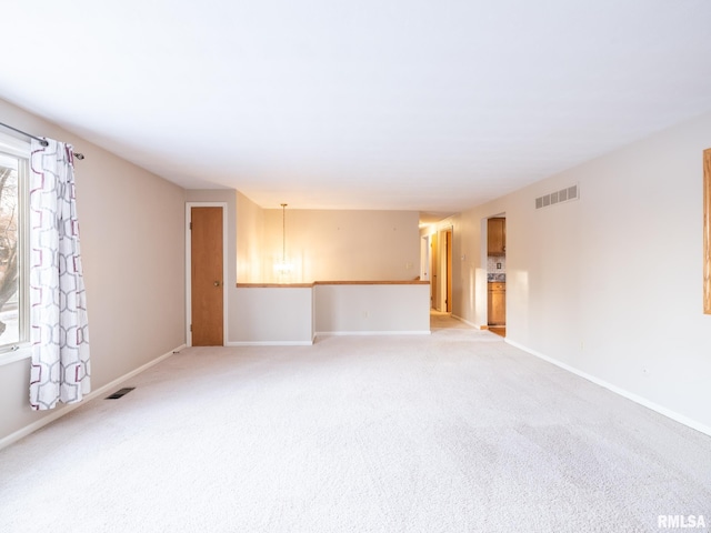 spare room featuring light carpet and an inviting chandelier