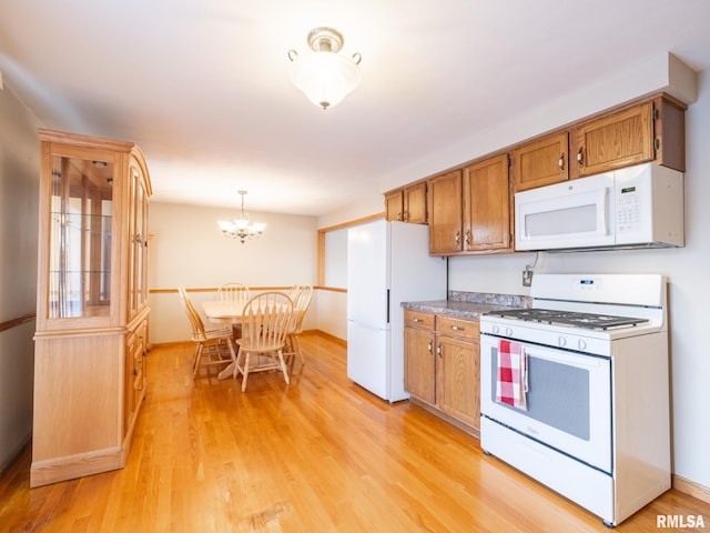 kitchen featuring a notable chandelier, light wood-type flooring, white appliances, and hanging light fixtures