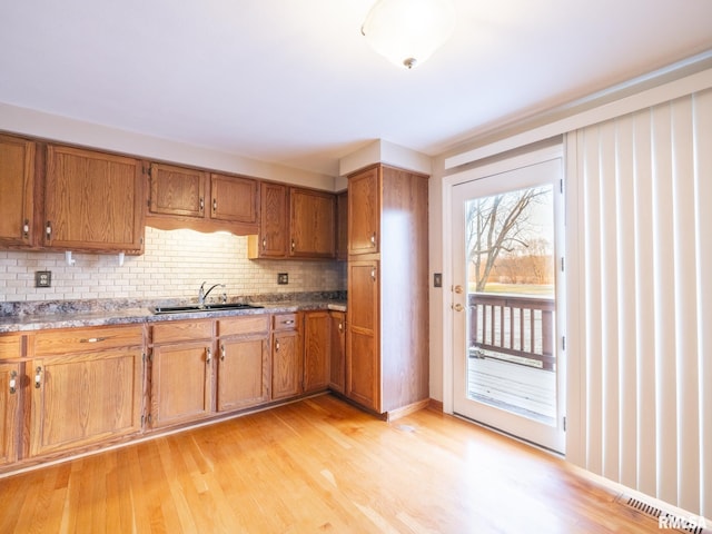 kitchen featuring decorative backsplash, sink, stone countertops, and light wood-type flooring