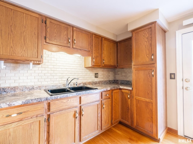 kitchen featuring backsplash, light stone countertops, light wood-type flooring, and sink