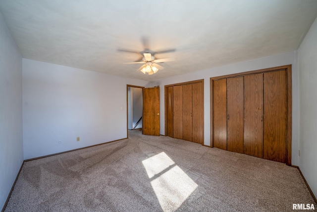 unfurnished bedroom featuring carpet flooring, two closets, a ceiling fan, and baseboards