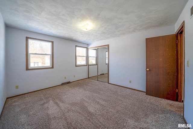 unfurnished bedroom with a textured ceiling, carpet floors, visible vents, and baseboards