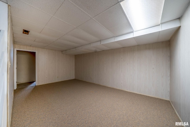 spare room with light colored carpet, wooden walls, and a drop ceiling