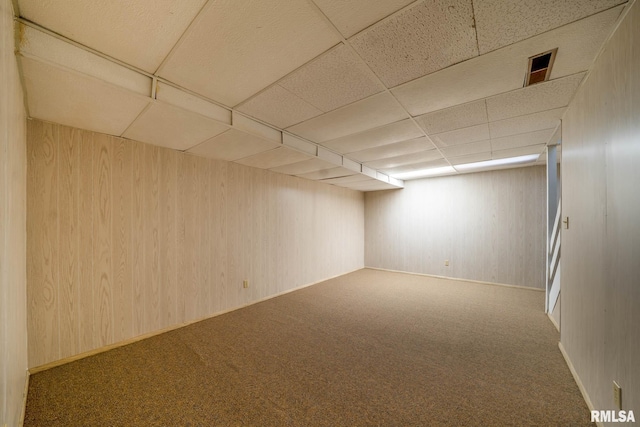 finished below grade area with wooden walls, a drop ceiling, and carpet flooring