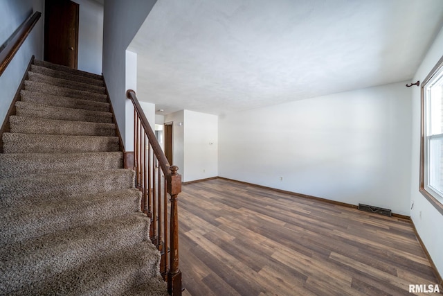 staircase with baseboards, visible vents, and wood finished floors