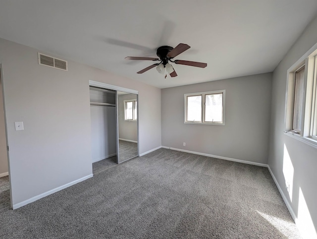 unfurnished bedroom with a closet, carpet flooring, multiple windows, and ceiling fan