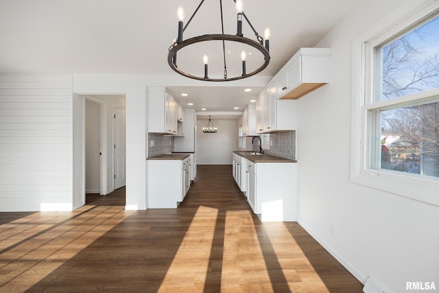 kitchen with tasteful backsplash, sink, white cabinets, dark hardwood / wood-style floors, and hanging light fixtures