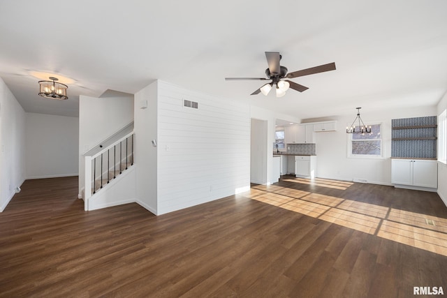 unfurnished living room featuring ceiling fan with notable chandelier and dark wood-type flooring