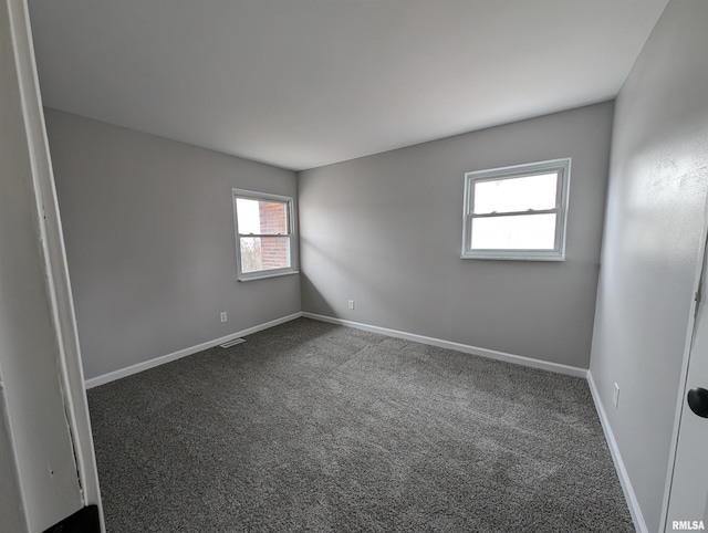 spare room with dark colored carpet, visible vents, and baseboards