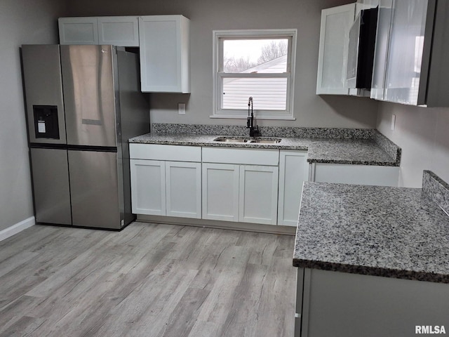 kitchen with light stone counters, a sink, white cabinets, and stainless steel fridge with ice dispenser