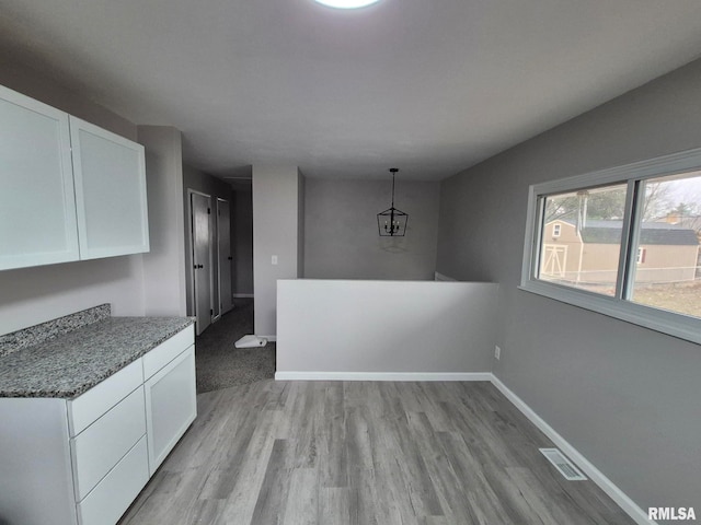 unfurnished dining area with light wood-type flooring, baseboards, visible vents, and a notable chandelier