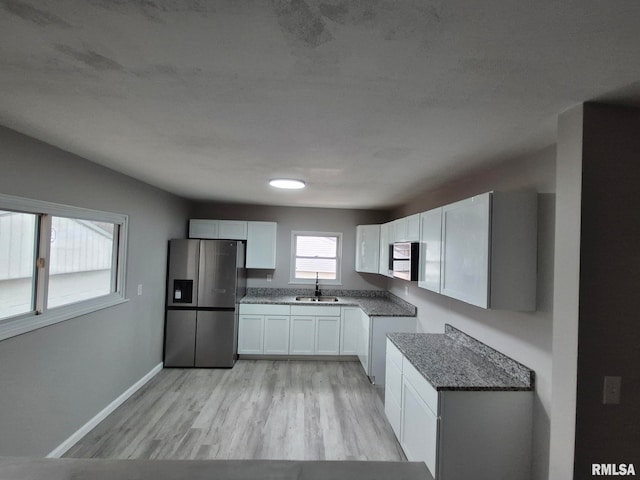 kitchen featuring stainless steel fridge, baseboards, light wood-type flooring, white cabinetry, and a sink