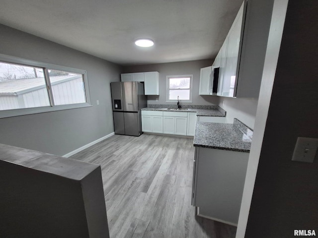 kitchen featuring stone countertops, a sink, white cabinetry, stainless steel refrigerator with ice dispenser, and light wood finished floors