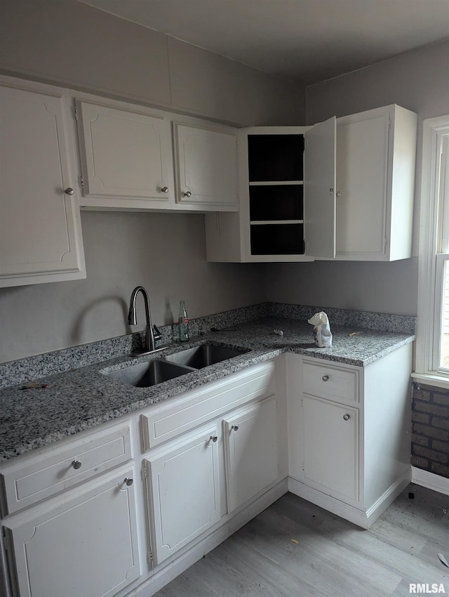 kitchen featuring light hardwood / wood-style floors, sink, white cabinetry, and light stone counters