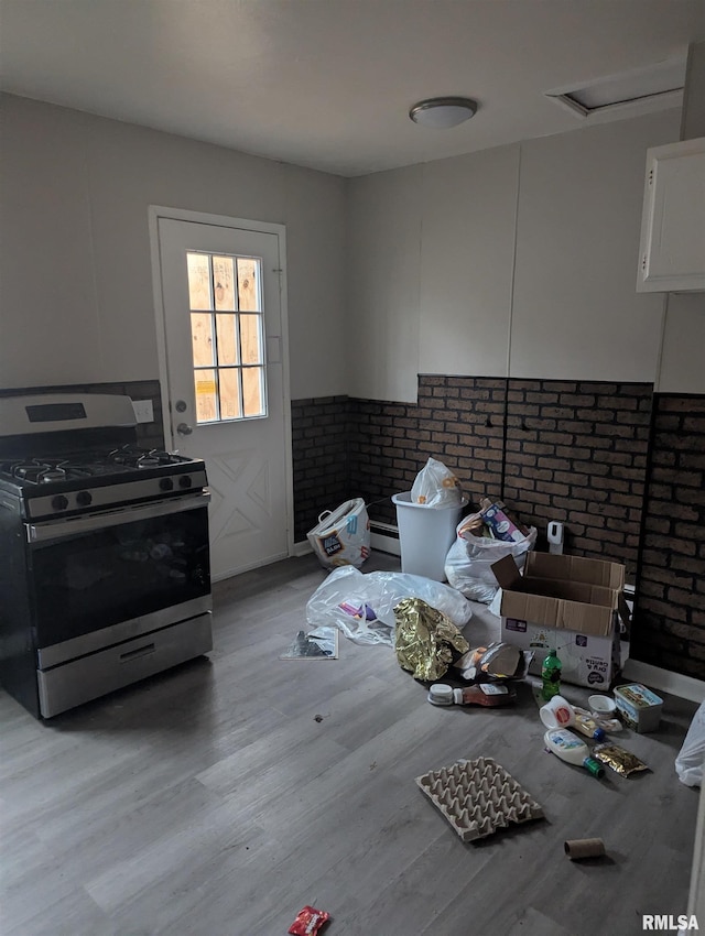 kitchen featuring brick wall, white cabinets, stainless steel gas range, and light hardwood / wood-style flooring