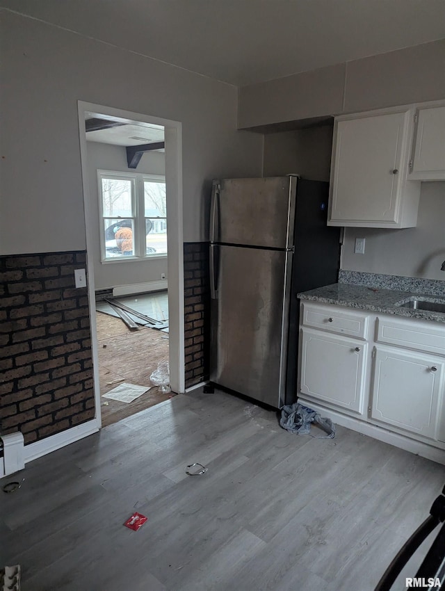 kitchen with light wood-type flooring, sink, stainless steel refrigerator, and white cabinetry