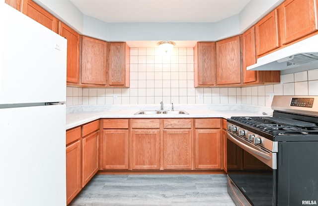 kitchen with backsplash, gas stove, sink, white refrigerator, and light hardwood / wood-style floors