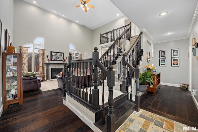 staircase featuring hardwood / wood-style floors, ceiling fan, crown molding, and a high ceiling