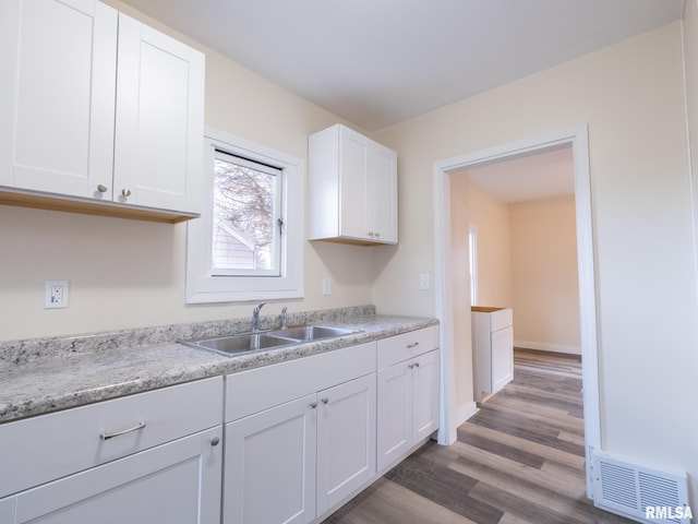 kitchen featuring light stone countertops, hardwood / wood-style flooring, white cabinetry, and sink