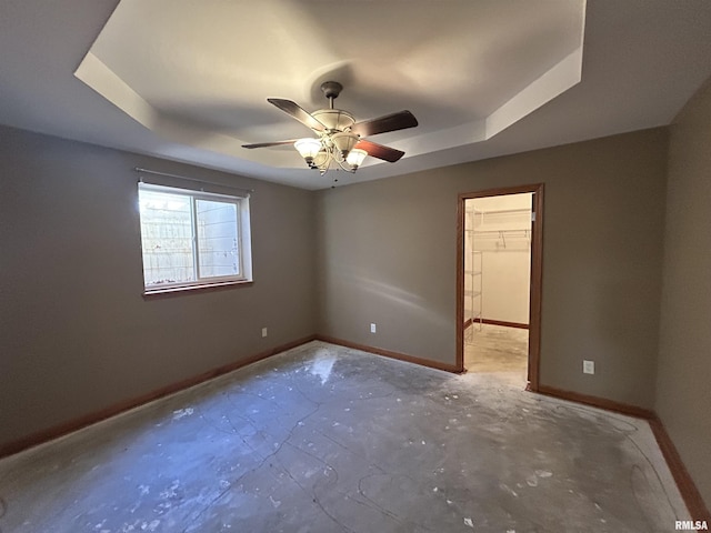 spare room with ceiling fan, concrete floors, and a tray ceiling