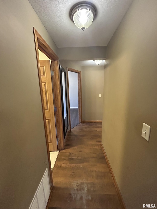 corridor with a textured ceiling and dark wood-type flooring