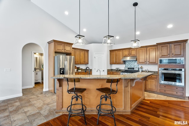 kitchen featuring light stone countertops, appliances with stainless steel finishes, a breakfast bar, a kitchen island with sink, and hanging light fixtures