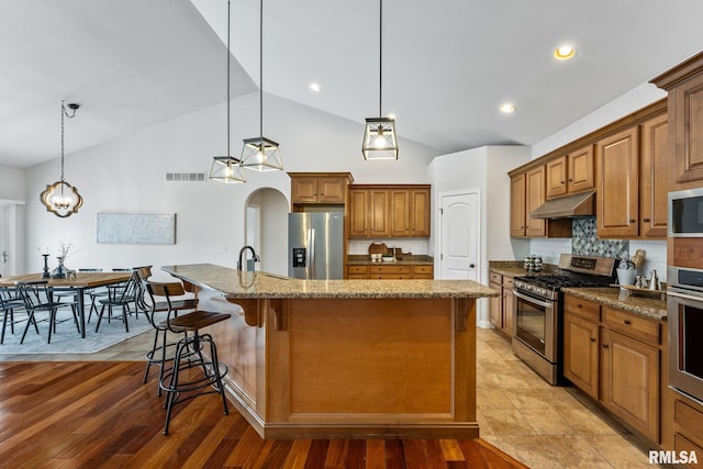 kitchen featuring backsplash, a kitchen island with sink, hanging light fixtures, and appliances with stainless steel finishes