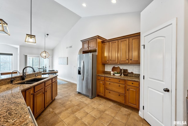 kitchen featuring sink, hanging light fixtures, backsplash, dark stone countertops, and stainless steel fridge