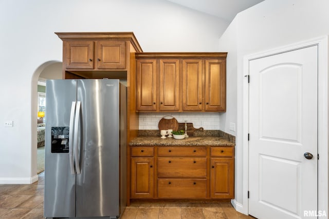 kitchen featuring decorative backsplash, stainless steel fridge with ice dispenser, and dark stone countertops