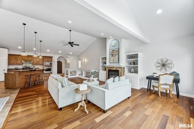 living room with high vaulted ceiling, ceiling fan, a high end fireplace, and light hardwood / wood-style flooring