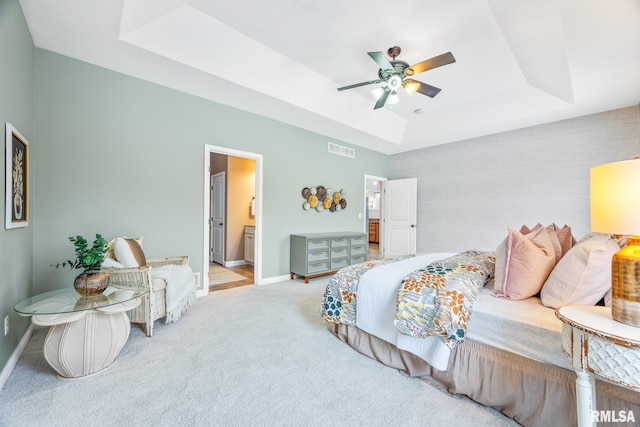 bedroom with light carpet, a tray ceiling, ensuite bath, and ceiling fan