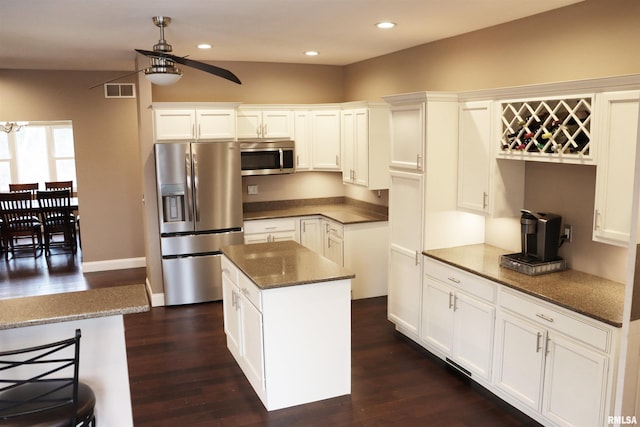 kitchen featuring appliances with stainless steel finishes, a kitchen island, ceiling fan, dark stone countertops, and white cabinetry