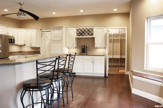 kitchen featuring a breakfast bar, stainless steel appliances, ceiling fan, dark stone countertops, and white cabinets